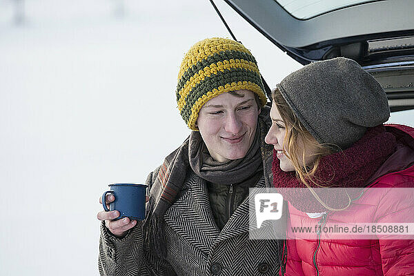 Young couple sitting on the trunk of a car with a coffee cup in winter  Bavaria  Germany