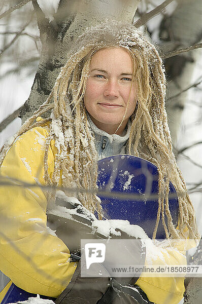 Young woman with dreadlocks holding snowboard.
