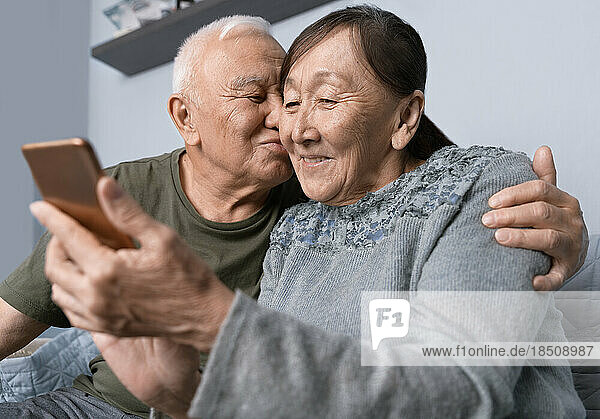 Senior couple using smartphone. Senior man kissing his wife