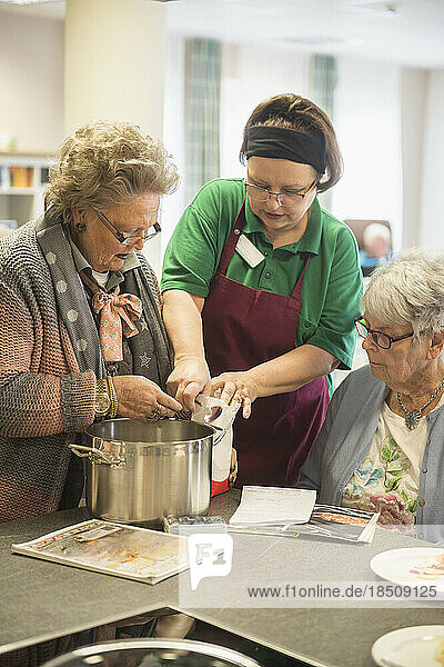 Nurse with senior women preparing food at rest home
