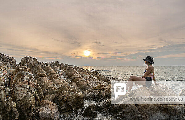 traveler woman enjoying sunset alone on rocky beach
