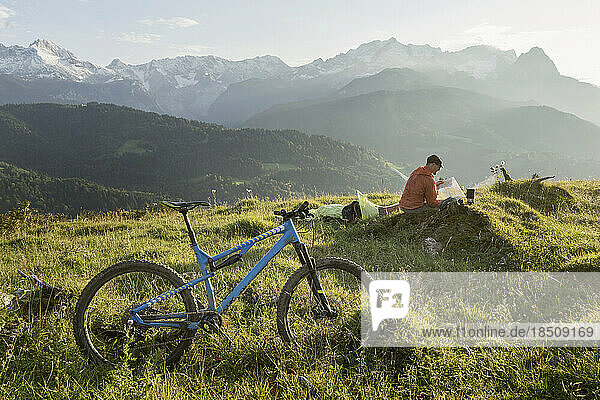 Mountain biker relaxing on alpine landscape and looking at map  Bavaria  Germany