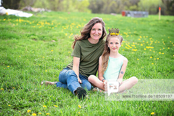Mother and daughter sitting together in a dandelion meadow.