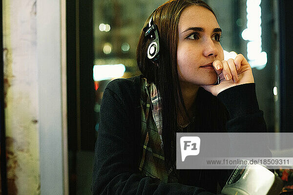 Thoughtful young woman listening music in headphones sitting in cafe