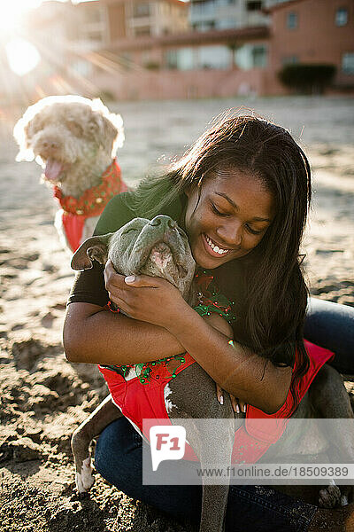 Young girl hugging pitbull on beach at sunset