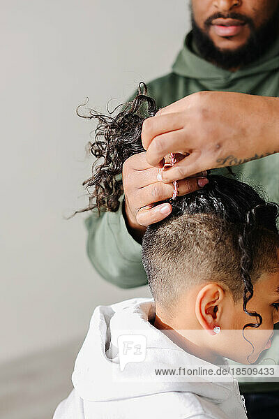 Close up of Black dad putting biracial son's hair in pony tail
