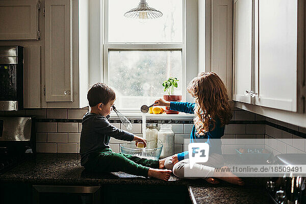 Young boy and girl sitting on counter in kitchen mixing muffin batter