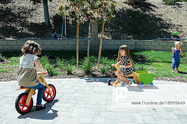 Two little girls ride wooden push bikes outside