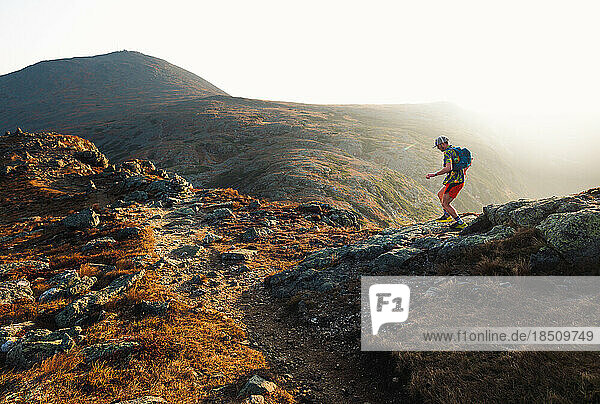 Male trail runners running along trail at sunrise in mountains
