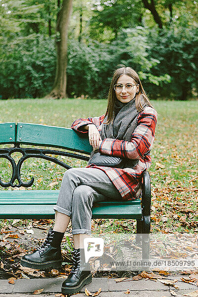 young woman in a warm coat sits on a bench in an autumn park