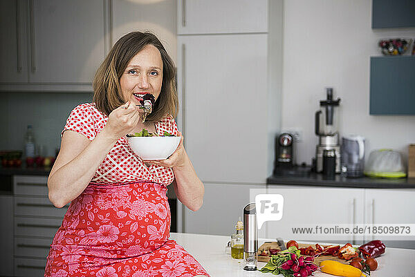 Portrait of a pregnant woman eating salad in the kitchen  Munich  Bavaria  Germany