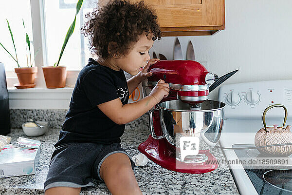 Biracial boy toddler peering into mixing bowl from counter
