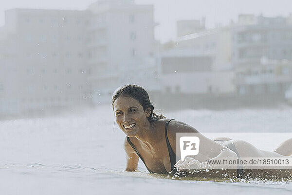 A female surfer smiles while paddling in sea