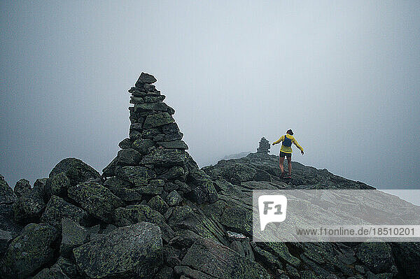 Woman running ridge with cairns in early morning fog