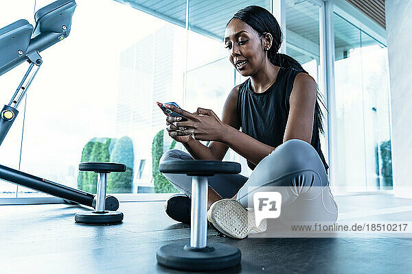 An african-american woman sitting in the gym - using her phone