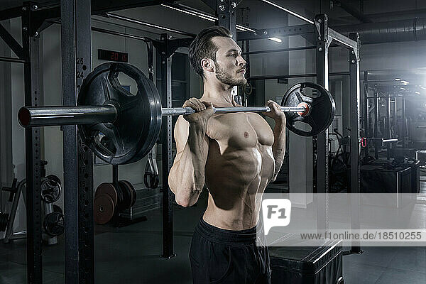 Shirtless muscular man exercising with barbell at the gym