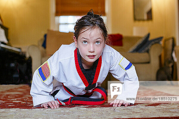 A fierce girl in Taekwondo uniform does pushups in living room