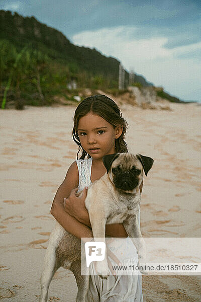 Girl child holding a pug dog in her arms on the ocean.