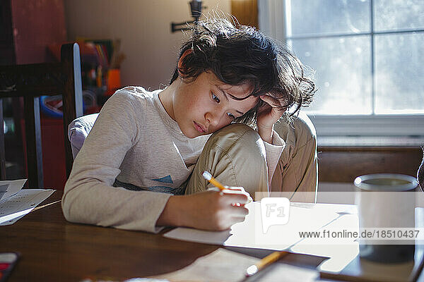 A child with head in hands focuses on schoolwork at home