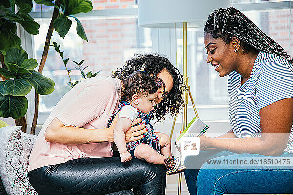 Side view of smiling mothers showing picture book to cute son while sitting at home