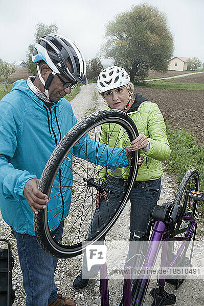 Senior couple adjusting wheel of cycle on dirt road  Bavaria  Germany