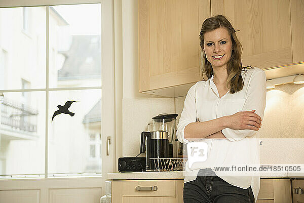 Young woman standing with arms crossed in kitchen and smiling  Munich  Bavaria  Germany