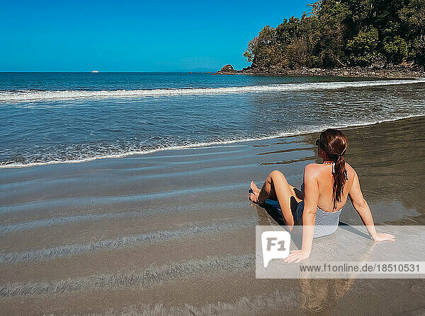 Woman in swimsuit sitting on a sandy beach in sunny Costa Rica.