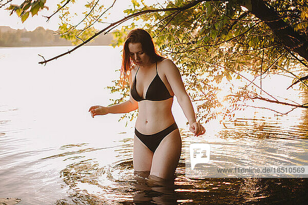 Young woman in a bikini standing in lake under tree