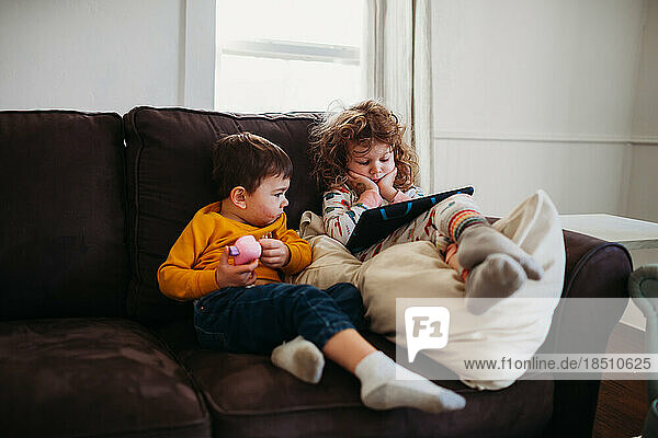 Young girl and boy sitting on couch together watching tablet