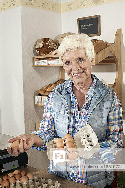 Portrait of a vendor arranging eggs in egg carton in the shop and smiling  Bavaria  Germany