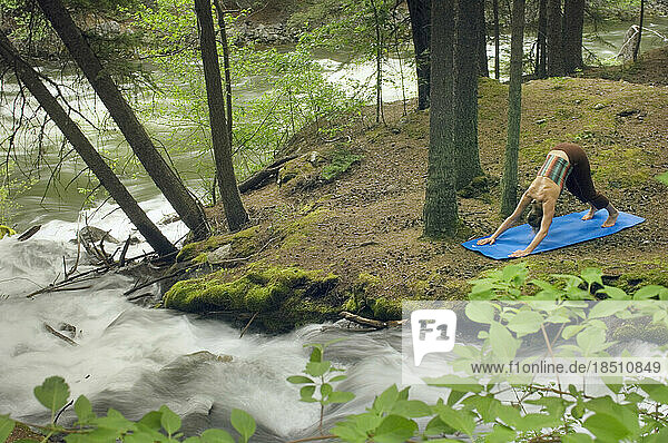 Woman practicing yoga by mountain stream.