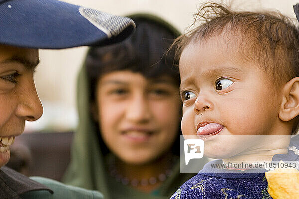 A baby sticks out its tongue at another child in Kabul.