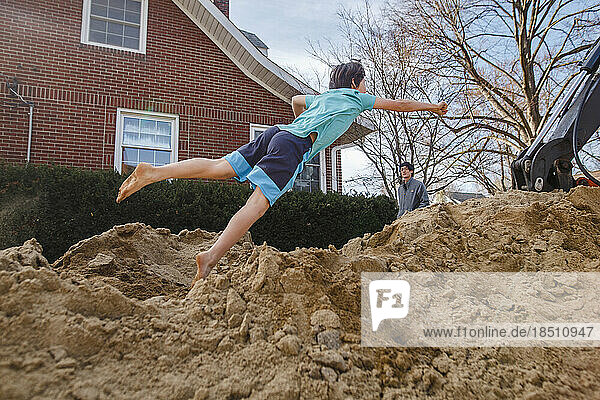 A barefoot boy leaps into giant pile of sand while father looks on