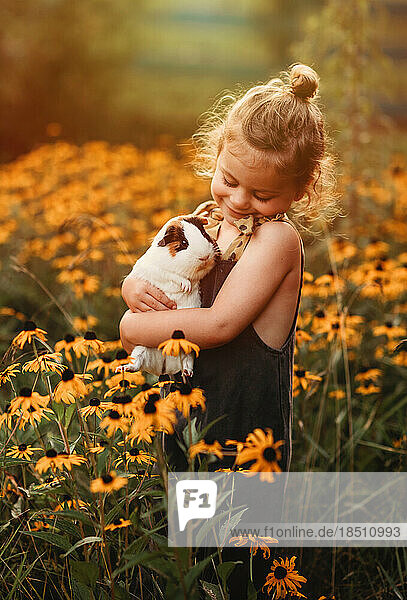 little girl snuggling her pet guinea pig in a field of flowers
