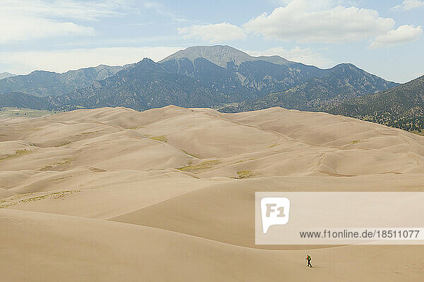 Man hikes across sand dunes with mountains in background
