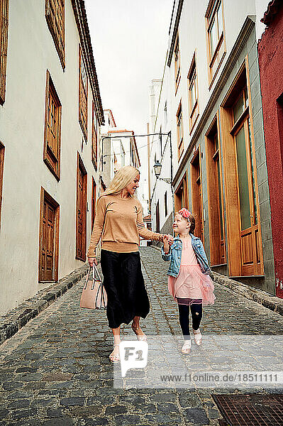 Mother and daughter walking down narrow cobbled street holding hands
