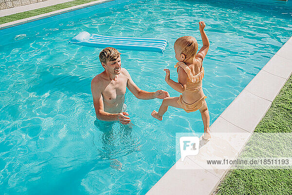 A two-year-old girl jumps from the side into the outdoor pool