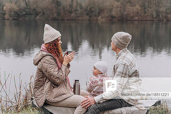 Parents and a little girl are relaxing in a spring park near the river
