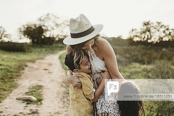 Young mother in hat being hugged by small children in field