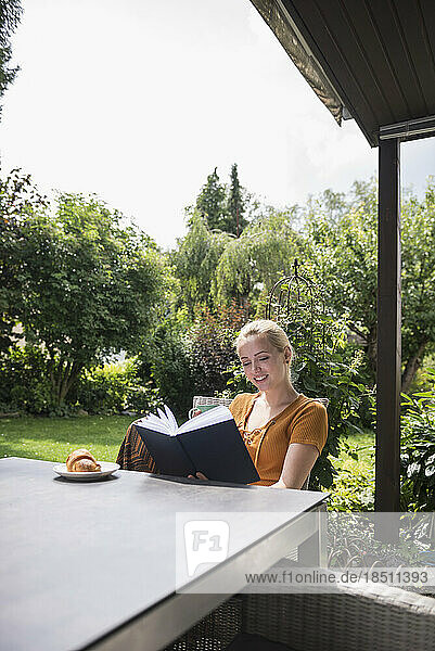 Beautiful young woman having cup of tea and reading book in the domestic garden  Munich  Bavaria  Germany