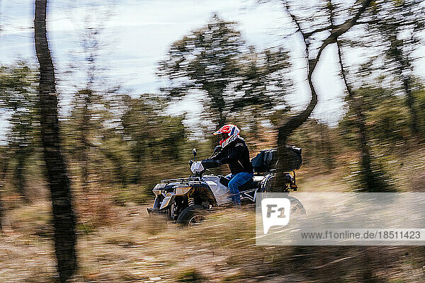 Sweeping stock photo of man riding a quad bike between forest