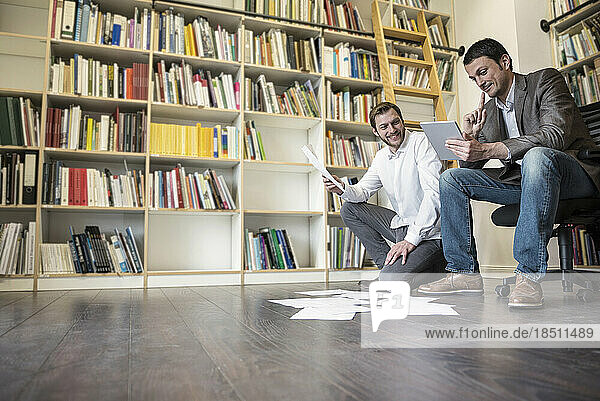 Two businessmen looking at notes and using digital tablet in an office  Bavaria  Germany