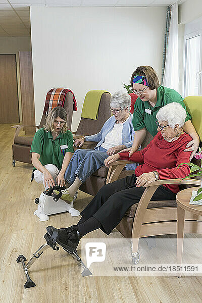 Nurse helping senior women doing exercise on mini foot pedal in rest home