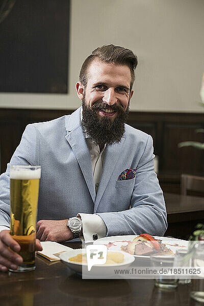 Well-dressed man holding beer glass and eating food at restaurant
