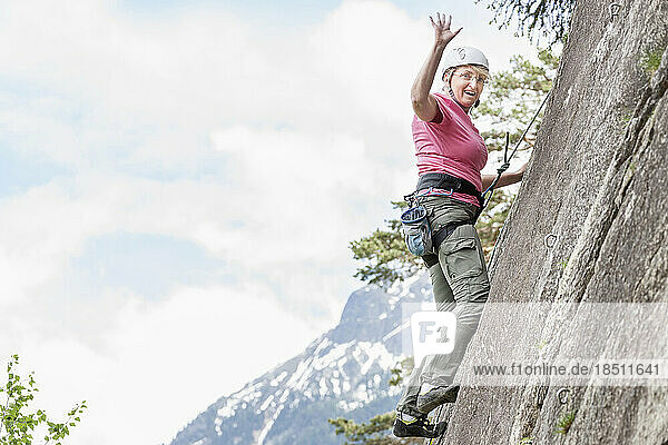 Female rock climber scaling a rock face and waving at Oberried climbing garden  Otztal  Tyrol  Austria