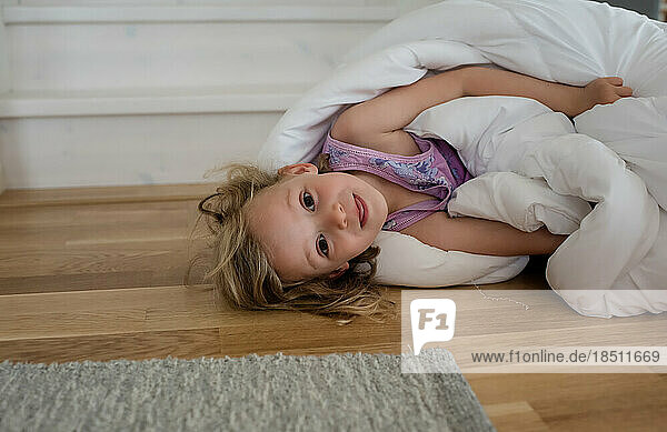 portrait of a young blond girl playing in a duvet on the floor at home