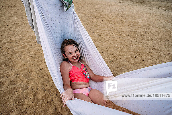 Happy young girl swinging in hammock on beach