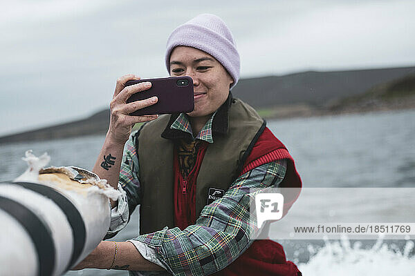 Asian person takes photo with phone on back of boat in Scotland