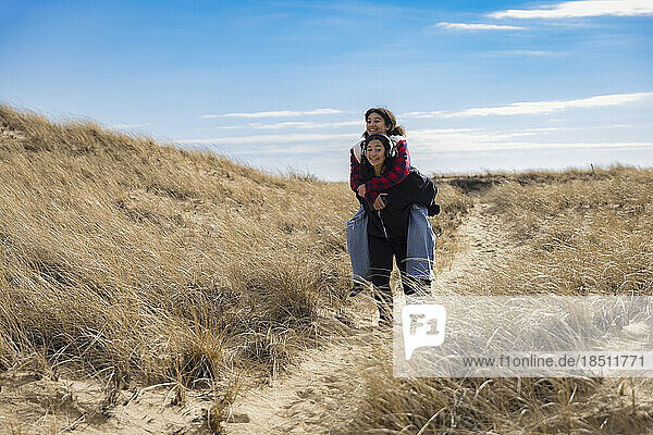biracial teen sisters piggy-back riding and smiling on sandy path