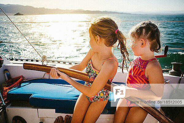 Two young girls steer sailboat on lake with sunshine in summer